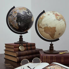 Two world globes on a table with books and glasses.