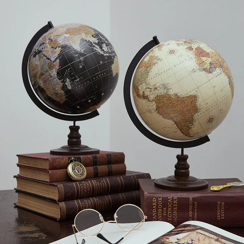 Two world globes on a table with books and glasses.
