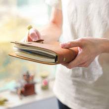 Person holding a brown leather notebook with a blurred indoor background