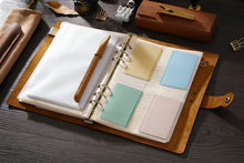 Open leather-bound planner with various inserts on a wooden surface